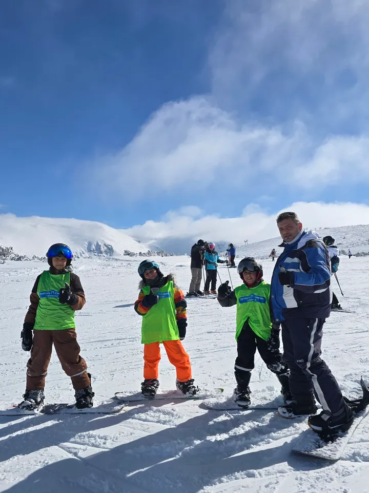 Παιδιά με σανίδες snowboard και προπονητής σε χιονισμένη πλαγιά